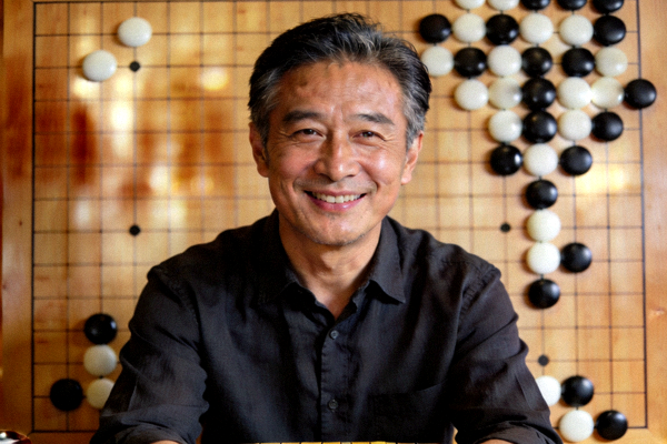 棋牌专家陈志远肖像照，中年男性面带微笑，背景为围棋棋盘，展示专业棋手形象